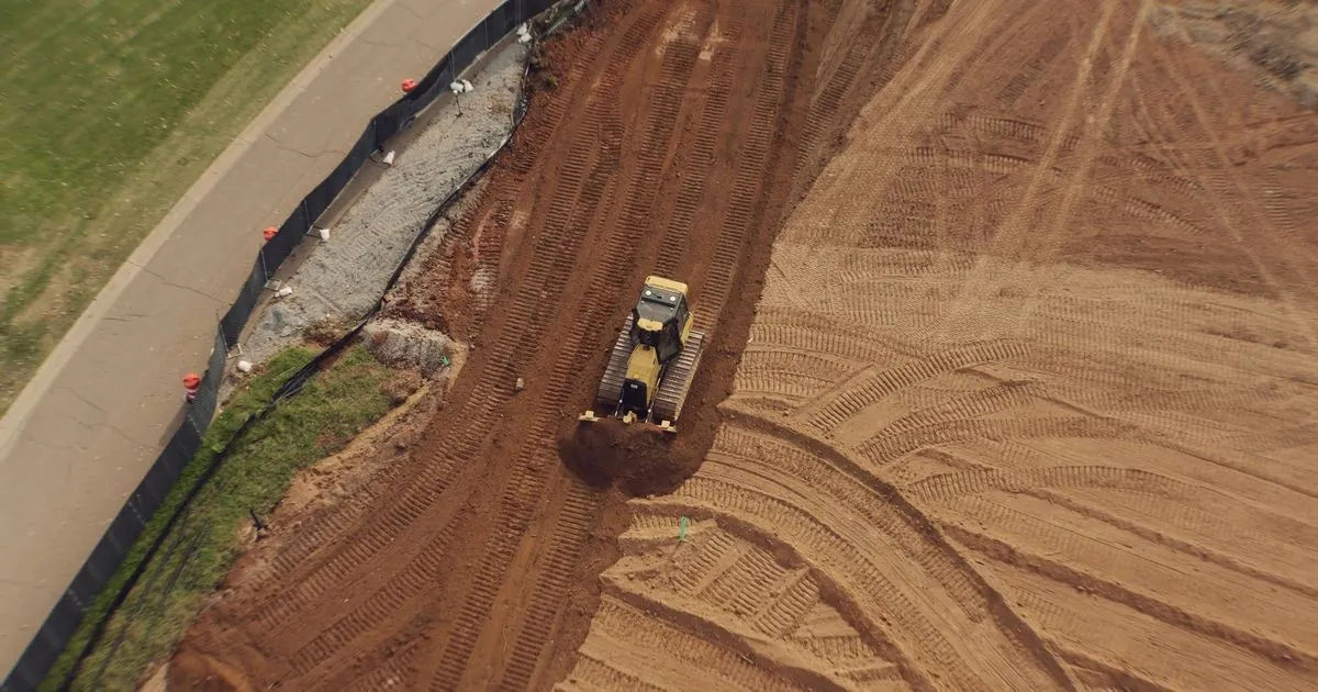 Niveleuse en train de terrasser le terrain d’une future carrière, vue du ciel
